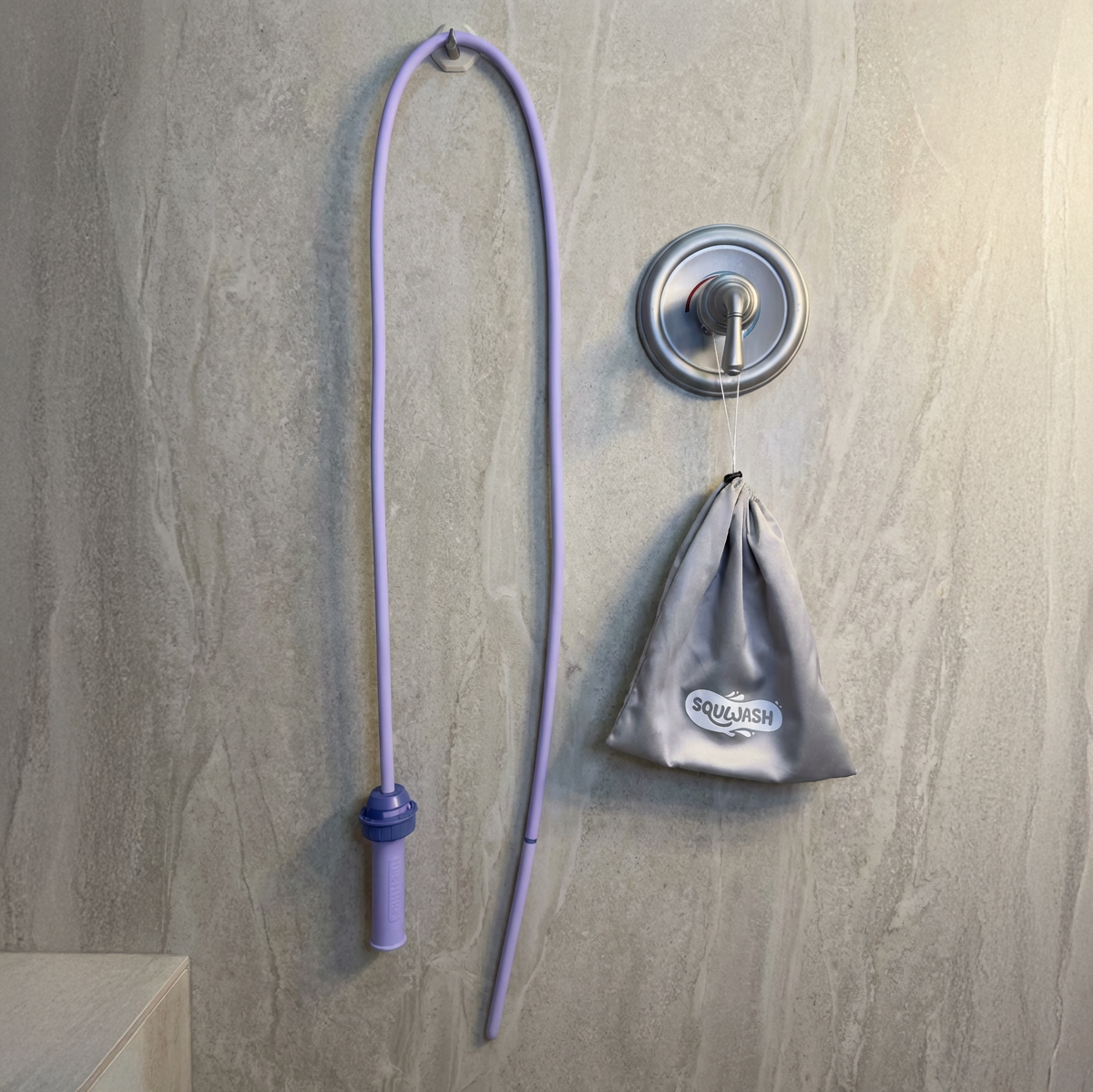 Purple Squwash device and silver satin travel bag hanging in modern bathroom setting against shower wall