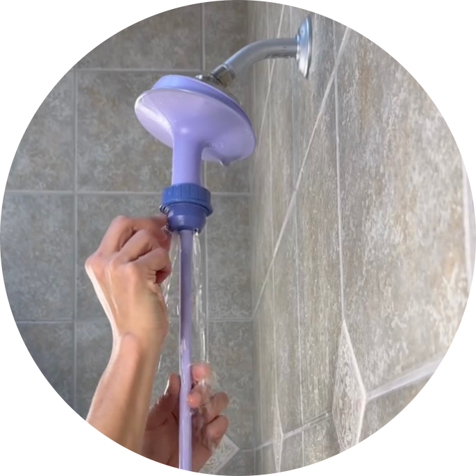 Person adjusting a shower pressure release valve on the Squwash portable shower douche while attached to shower against a tiled wall.