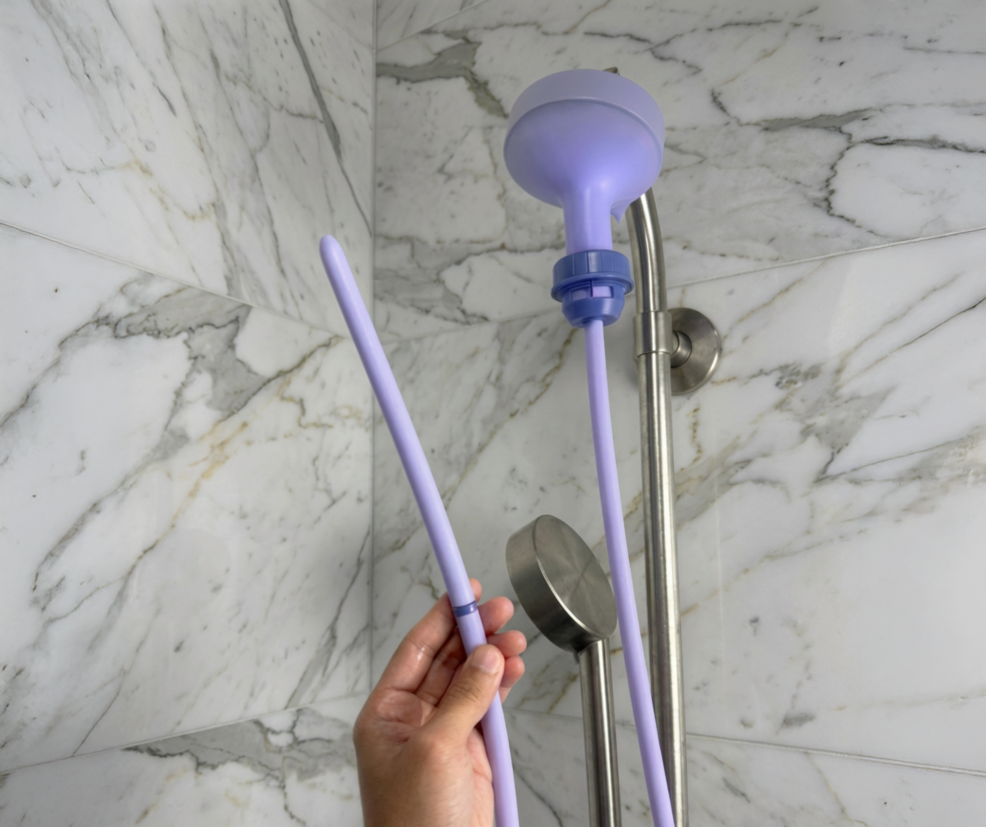 Purple Squwash Douche attached to shower head and hose held by a hand against a marble bathroom wall.