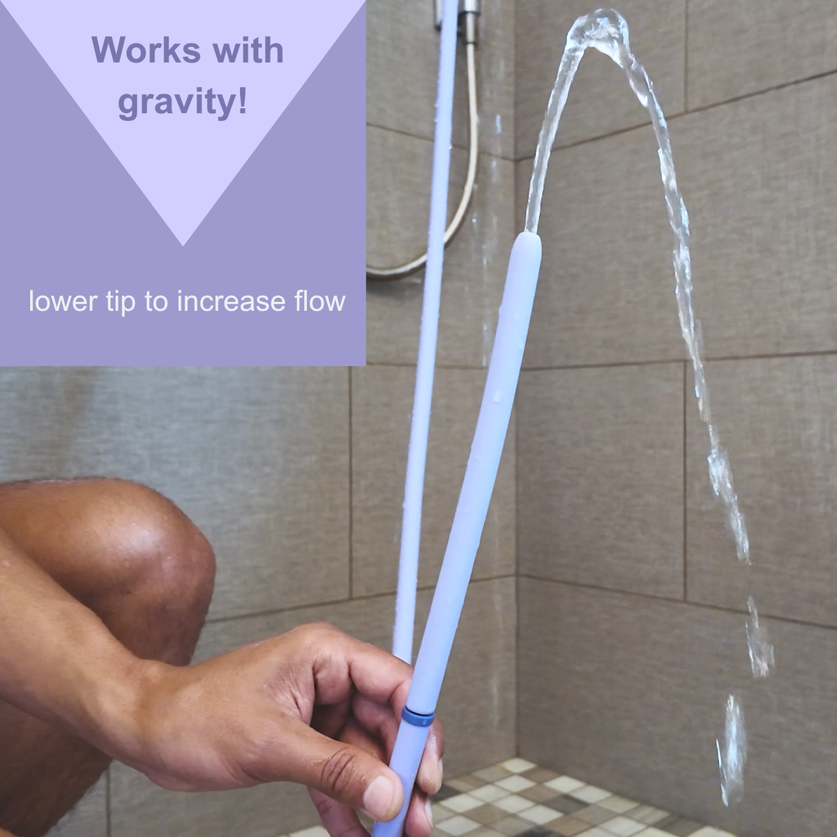 A person holds silicone wand tip of Squwash shower douche in a tiled bathroom, with water streaming from the tip. Text in the top left reads 'Works with gravity! lower tip to increase flow'.