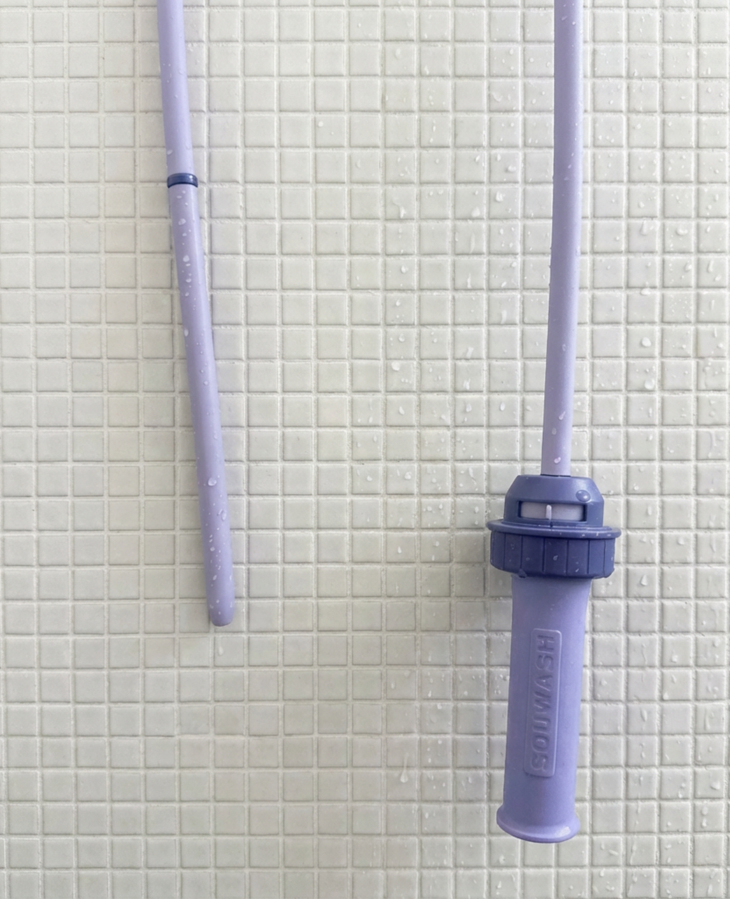 Squwash portable silicone shower douche enema kit showing up-close view of hose and patented connector against a white tile mosaic bathroom wall